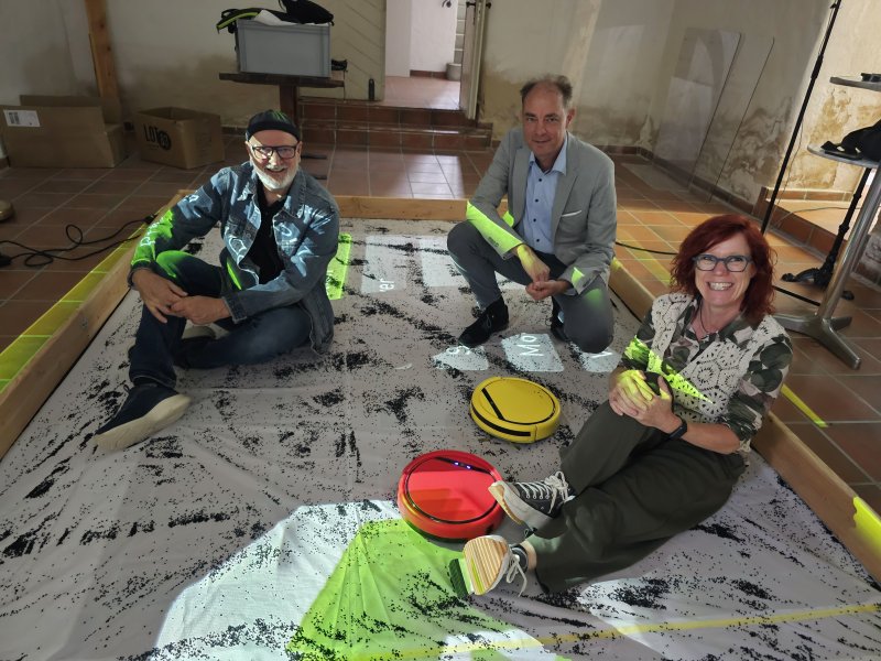 Drei Personen sitzen auf einer interaktiven Projektionsfläche mit Robotern. Event-Fotografie.