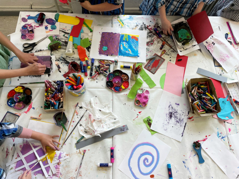 Kinder malen und basteln an einem Tisch. Farben, Papier und Kreativität im Kunstunterricht.