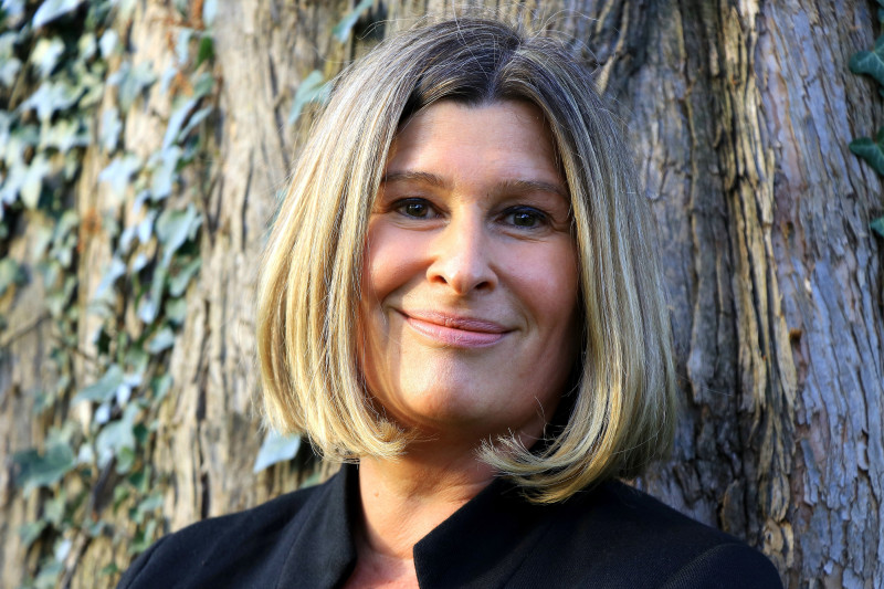 Porträt einer lächelnden Frau mit blonden Haaren vor einem Baum. Freundliches Business-Portrait im Freien.