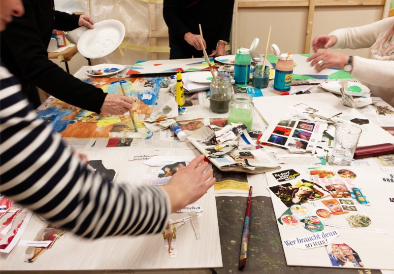 Kreative Gruppe beim Basteln von Collagen und Malen mit Acrylfarben im Kunstkurs auf einem unordentlichen Arbeitstisch.